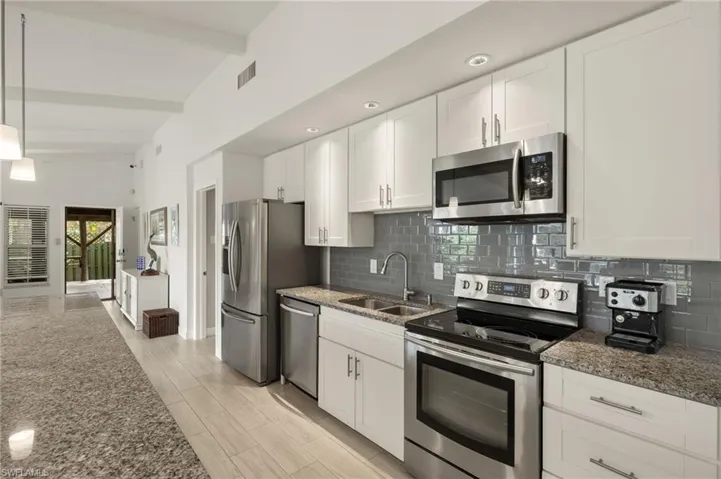 Kitchen featuring stainless steel appliances, white cabinetry, beamed ceiling, decorative backsplash, and light stone countertops