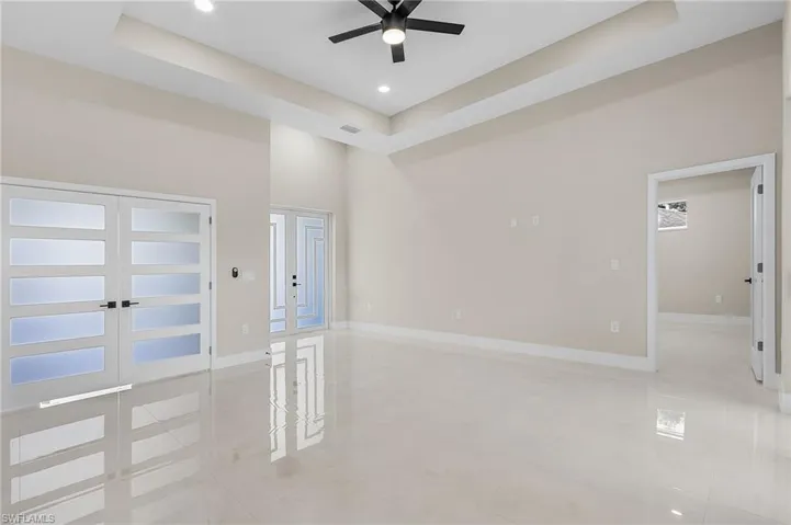 Tiled empty room featuring french doors, built in shelves, ceiling fan, a towering ceiling, and a raised ceiling