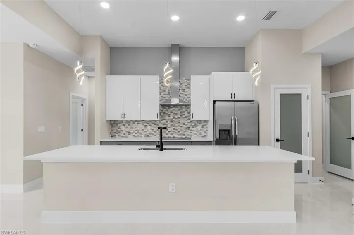 Kitchen featuring backsplash, wall chimney exhaust hood, stainless steel refrigerator with ice dispenser, and an island with sink