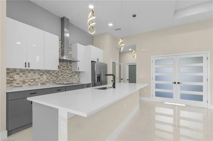 Kitchen with stainless steel refrigerator with ice dispenser, an island with sink, pendant lighting, and wall chimney range hood