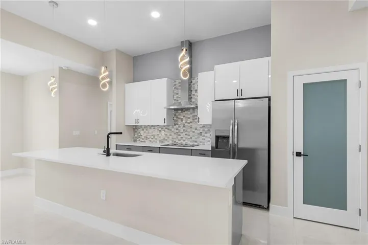 Kitchen with decorative backsplash, sink, a center island with sink, and stainless steel fridge