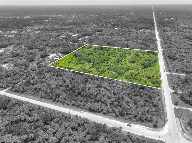 Aerial view of property and surrounding area featuring property parcel outlined and a heavily wooded area