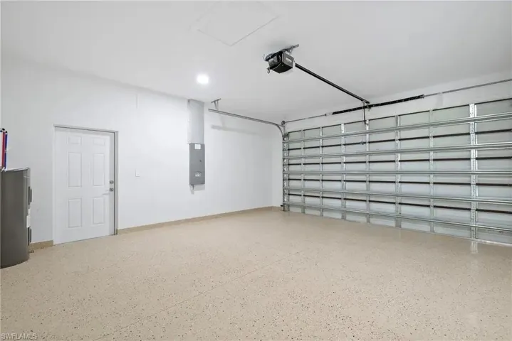 Garage featuring electric water heater, electric panel, and a garage door opener