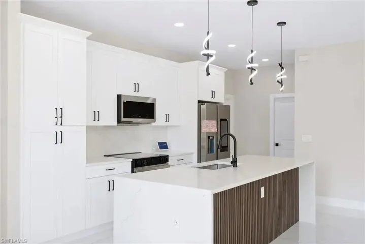 Kitchen featuring a center island with sink, stainless steel appliances, light stone counters, and white cabinetry