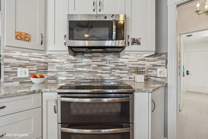 Kitchen featuring white cabinetry, backsplash, appliances with stainless steel finishes, and light stone counters
