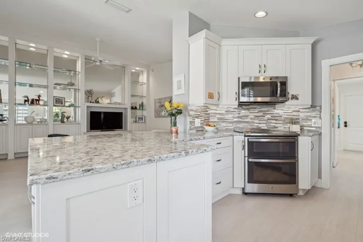 Kitchen with kitchen peninsula, light stone countertops, backsplash, appliances with stainless steel finishes, and white cabinets