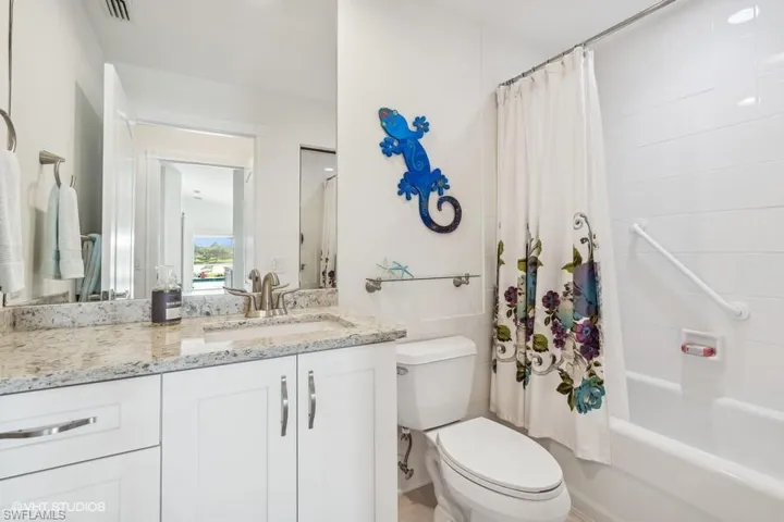 Full bathroom with tile walls, shower / bath combination with curtain, vanity, and toilet