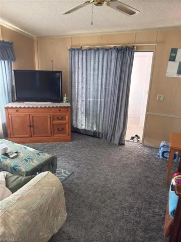 Living room featuring ceiling fan, a textured ceiling, and dark colored carpet
