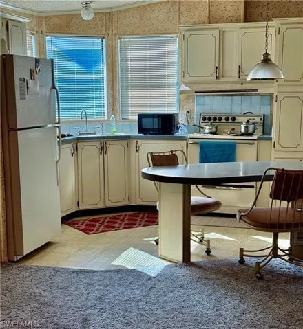 Kitchen featuring electric range, range hood, white fridge, cream cabinetry, and ornamental molding