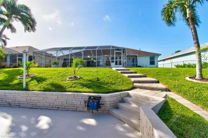 Back of house featuring screen enclosure, a lawn, and  paver walkway steps to dock