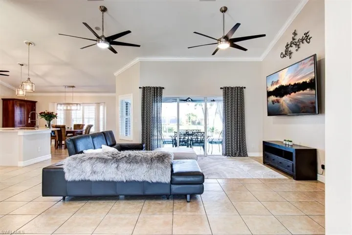 Living room with crown molding, healthy amount of natural light, light tile patterned flooring, ceiling fans, volume ceilings with crown molding.