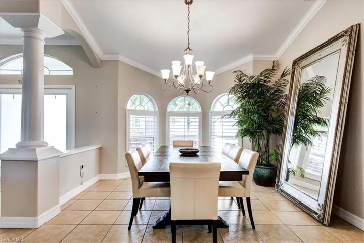 Dining room with ornamental molding, light tile patterned floors, a chandelier, and decorative columns