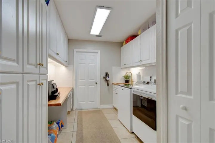 Laundry area with light tile patterned floors, separate washer and dryer, and ample cabinet space,butcher block tops, utility sink, storage closet.