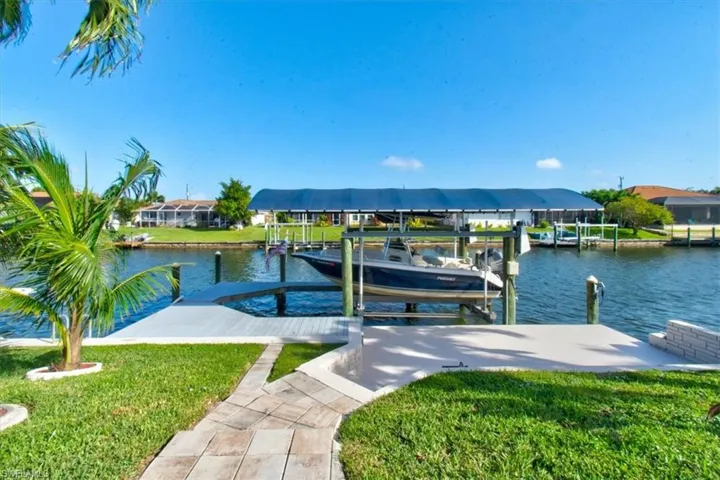 Dock featuring boat lift, a water view, a yard, and a residential view