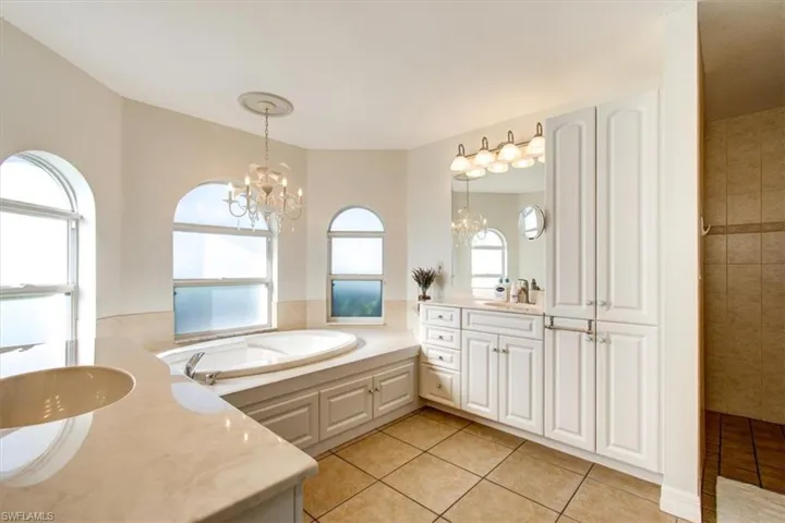 Full bath featuring two vanities, light tile patterned floors, a bath, a chandelier, and a tile shower