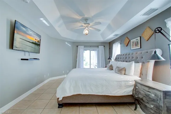 Bedroom with light tile patterned floors, a tray ceiling, and ceiling fan, door to pool.