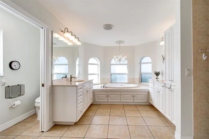Bathroom with light tile patterned flooring, vanity, a garden tub, and a chandelier