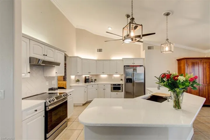 Kitchen with crown molding, roll out shelves, decorative light fixtures, appliances with stainless steel finishes, tasteful backsplash, quartz countertops