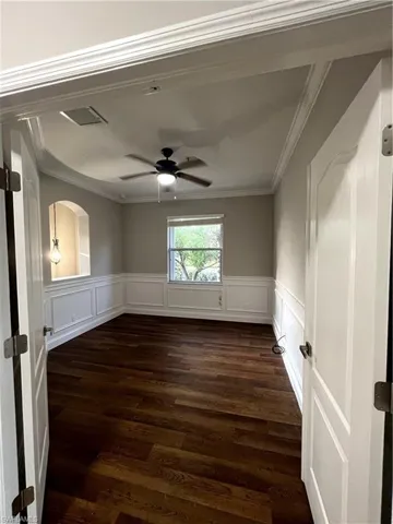 Empty room featuring dark wood-type flooring, a ceiling fan, wainscoting, and ornamental molding