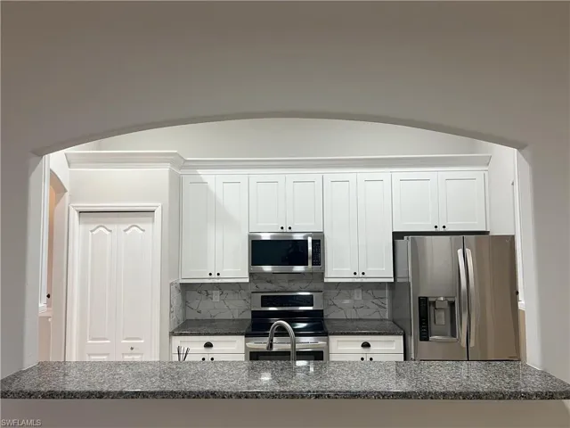 Kitchen with decorative backsplash, white cabinets, and appliances with stainless steel finishes