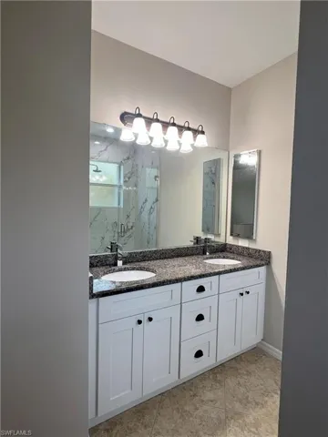 Bathroom featuring a sink, a marble finish shower, double vanity, and tile patterned flooring