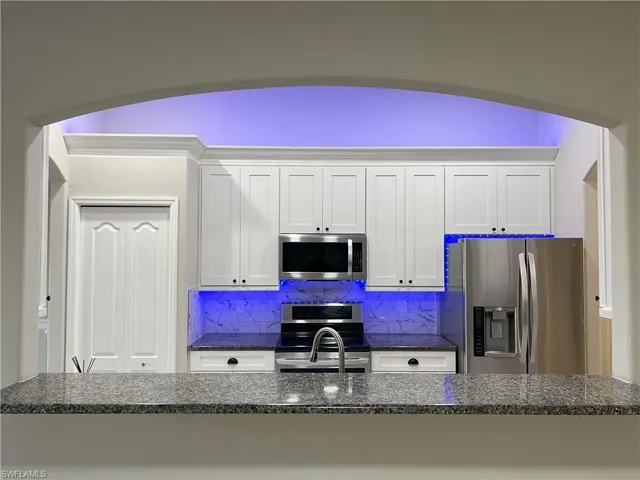Kitchen with tasteful backsplash, appliances with stainless steel finishes, and white cabinetry