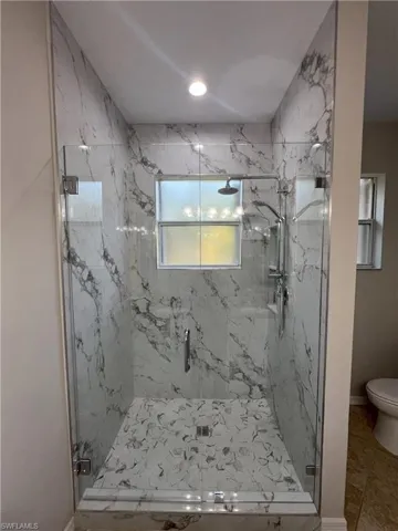 Bathroom with a marble finish shower, toilet, and baseboards