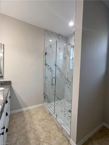 Full bathroom with a marble finish shower, recessed lighting, vanity, and baseboards