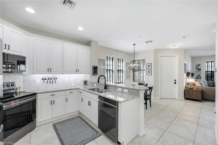 Kitchen featuring appliances with stainless steel finishes, light stone countertops, tasteful backsplash, a peninsula, and a chandelier
