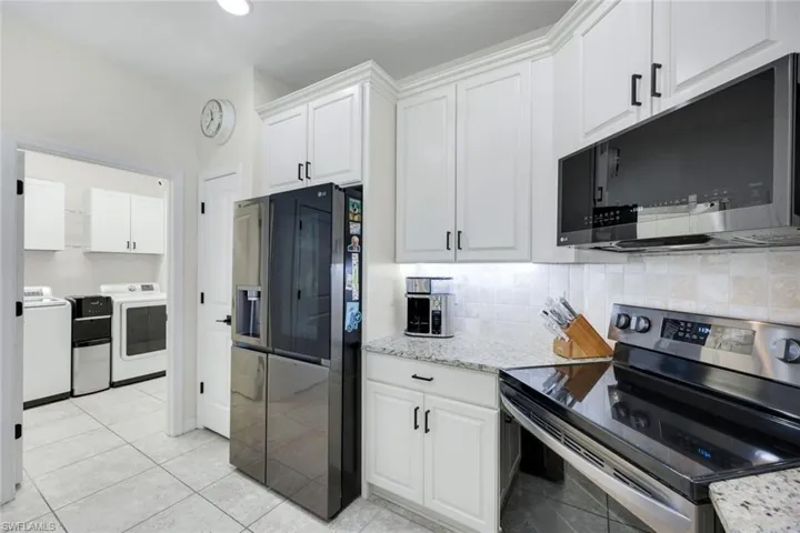 Kitchen with stainless steel appliances, white cabinets, light stone countertops, decorative backsplash, and washer and clothes dryer