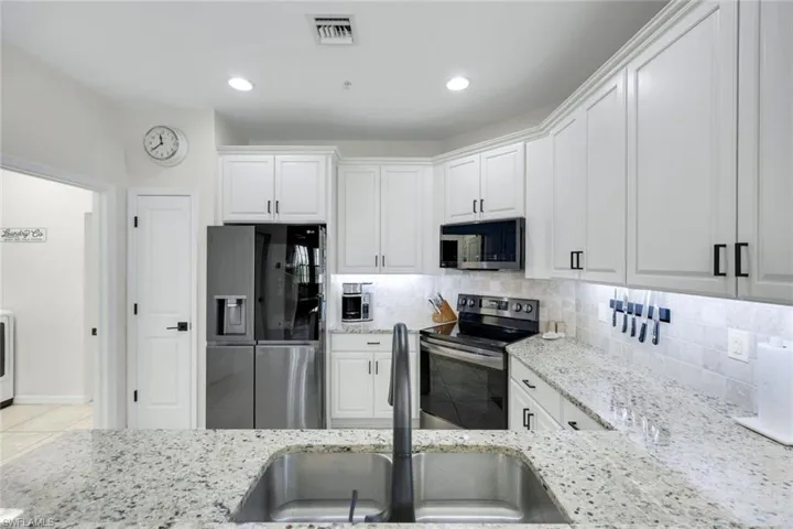 Kitchen featuring stainless steel appliances, backsplash, light stone counters, white cabinets, and recessed lighting