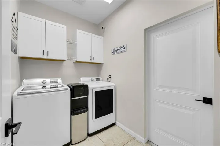 Washroom featuring washing machine and clothes dryer, cabinet space, and light tile patterned flooring