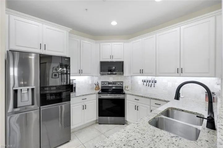 Kitchen with appliances with stainless steel finishes, tasteful backsplash, white cabinets, light stone countertops, and recessed lighting