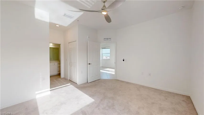 Unfurnished bedroom with light colored carpet, ensuite bathroom, ceiling fan, and a closet