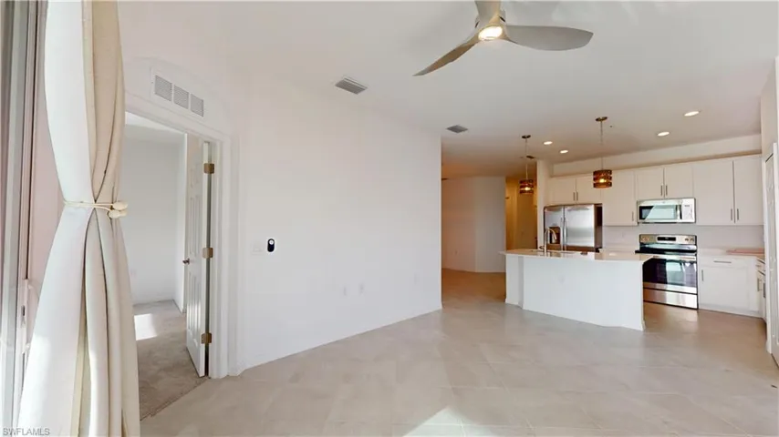 Kitchen featuring stainless steel appliances, open floor plan, hanging light fixtures, white cabinets, and a kitchen island with sink