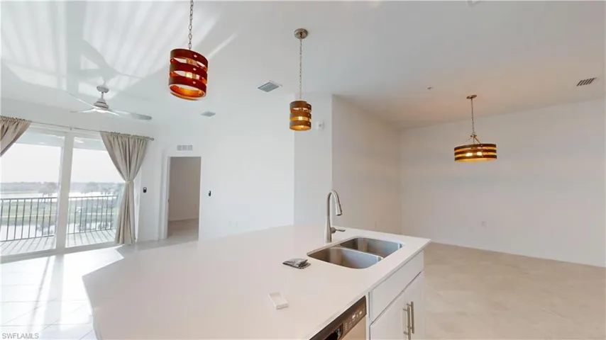 Kitchen featuring open floor plan, white cabinets, a kitchen island with sink, decorative light fixtures, and light stone counters