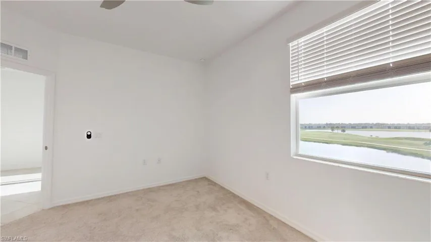 Empty room featuring light colored carpet, a ceiling fan, and a water view
