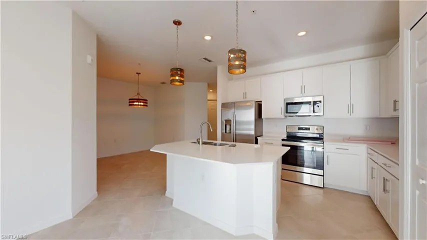 Kitchen with stainless steel appliances, a kitchen island with sink, pendant lighting, and white cabinets