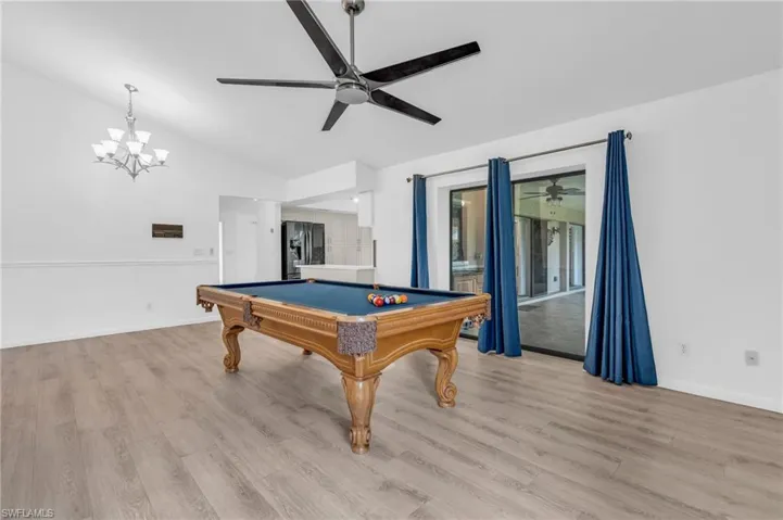 Recreation room featuring billiards, vaulted ceiling, ceiling fan with notable chandelier, and light wood-type flooring