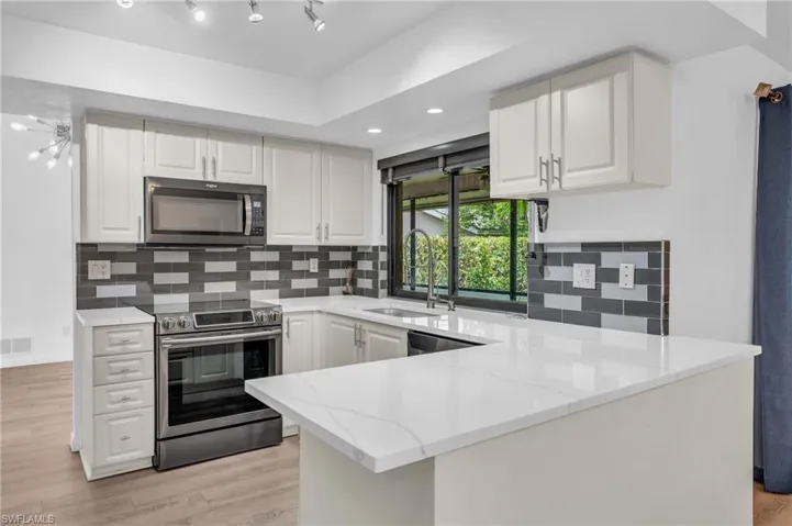 Kitchen with rail lighting, stainless steel appliances, light hardwood / wood-style flooring, and white cabinets