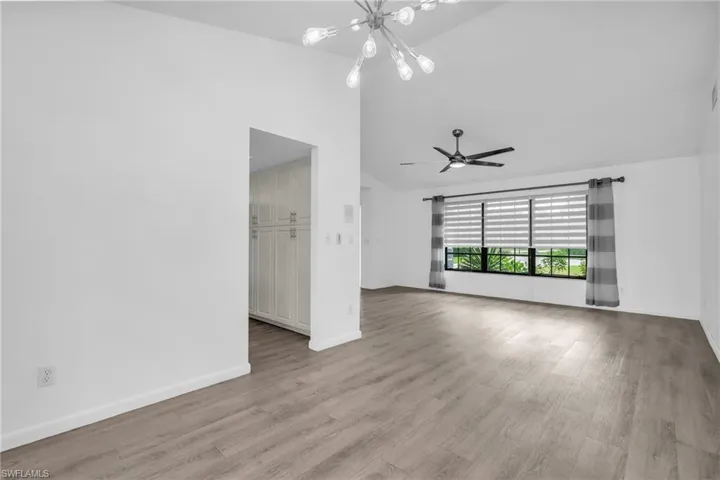 Empty room featuring light wood-type flooring, high vaulted ceiling, and ceiling fan with notable chandelier