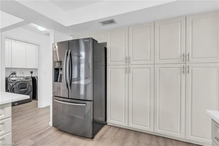 Kitchen with stainless steel fridge with ice dispenser, separate washer and dryer, light wood-type flooring, and white cabinets