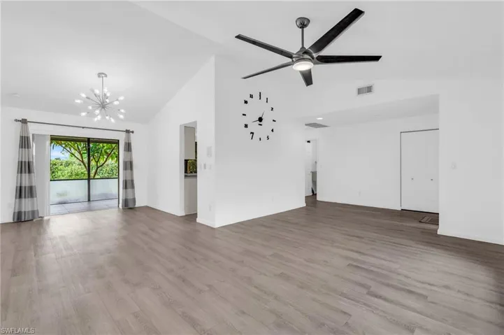 Unfurnished living room featuring light wood-type flooring, ceiling fan with notable chandelier, and high vaulted ceiling