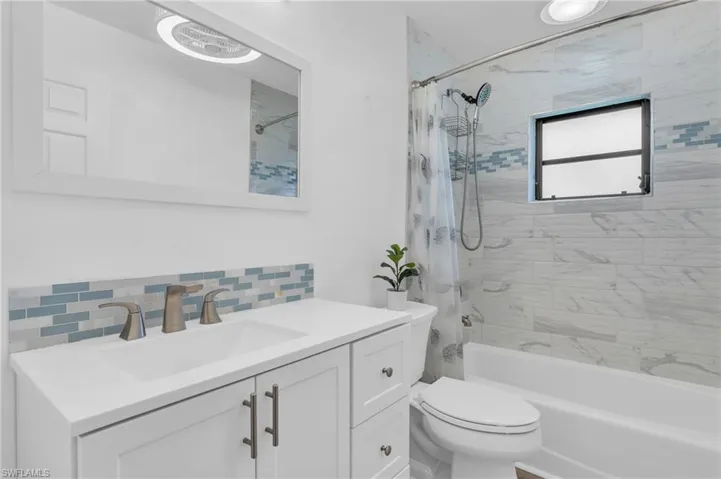 Full bathroom featuring decorative backsplash, toilet, vanity, tile walls, and shower / tub combo with curtain