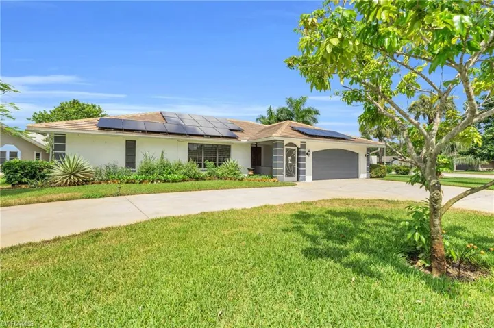 Ranch-style home featuring solar panels, a garage, and a front lawn