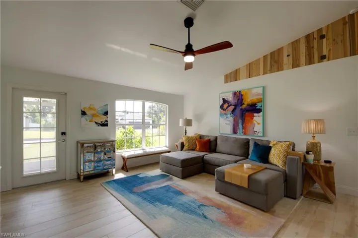 Living room with vaulted ceiling, wooden storage accent walls, ceiling fan, and light plank wood-style tile floors