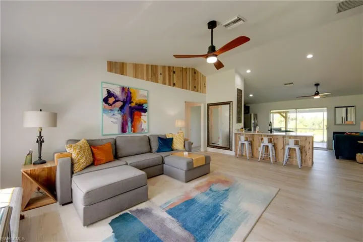 Living room with light porcelain plank wood- style flooring, ceiling fan, and high vaulted ceiling
