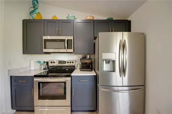 Kitchen with custom cabinets, granite cabinets, vaulted ceiling, stainless steel appliances, and tile decorative backsplash