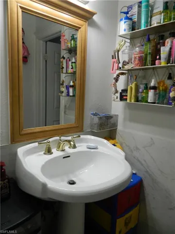 Wall-mounted mirror with a wood frame, white pedestal sink, and brass-finish widespread faucet