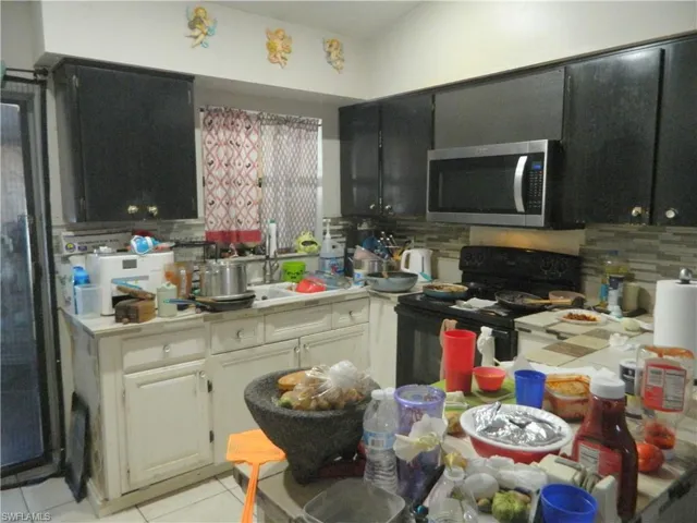 Kitchen featuring two-tone cabinetry, stainless steel over-the-range microwave, dual-basin sink with a pull-down faucet, and neutral tile backsplash